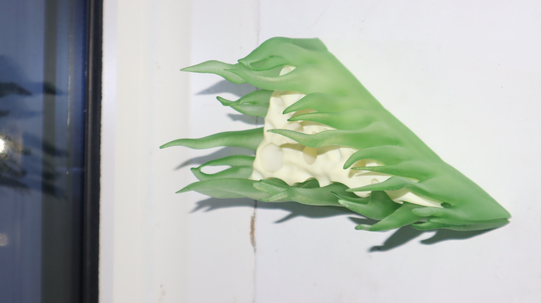 Full side view of the sculpture on a windowsill, showing its pointed end and curling green forms.