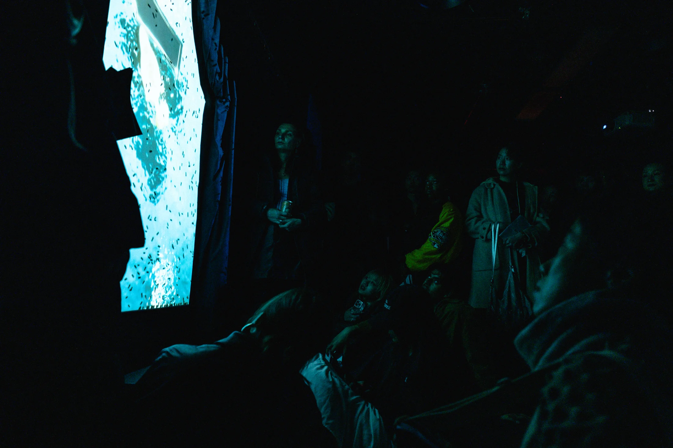 A luminous cyan figure projected beside a seated audience