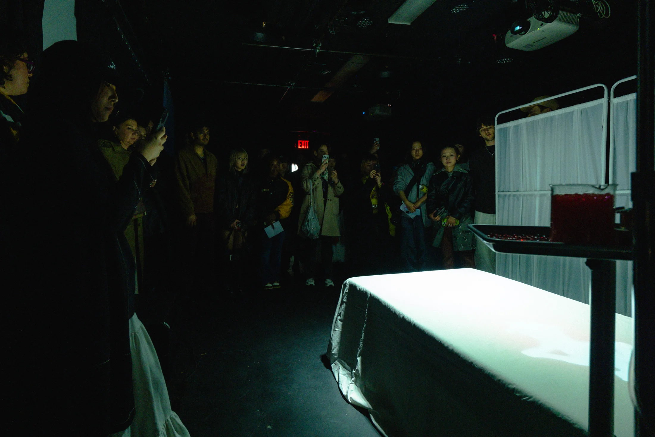 Audience members gathered around a white hospital bed in a dark performance space