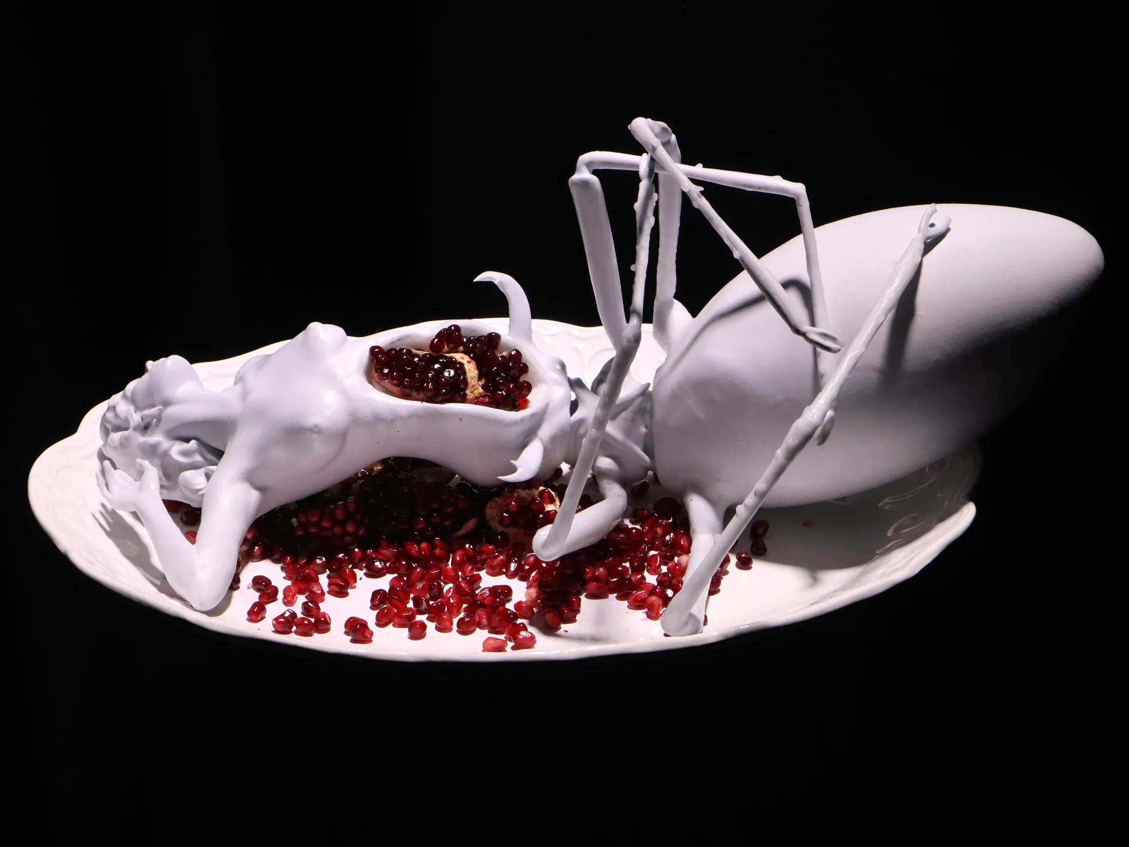 A white organic sculpture with long limbs and red seeds on a plate